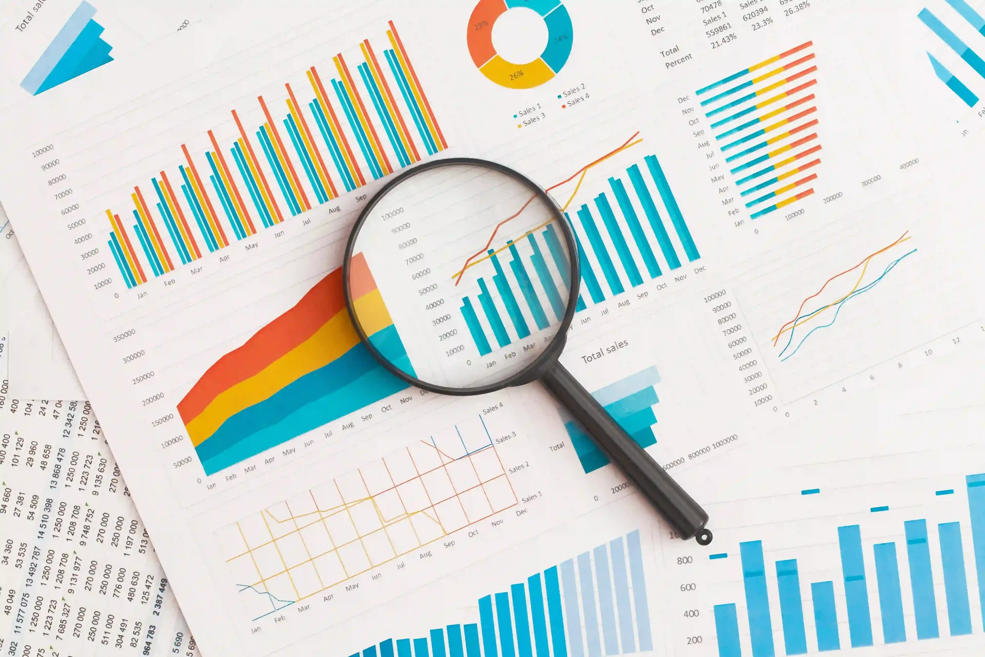 A black magnifying glass lying on several pieces of paper with different charts with statistical data. Web traffic analysis is important.