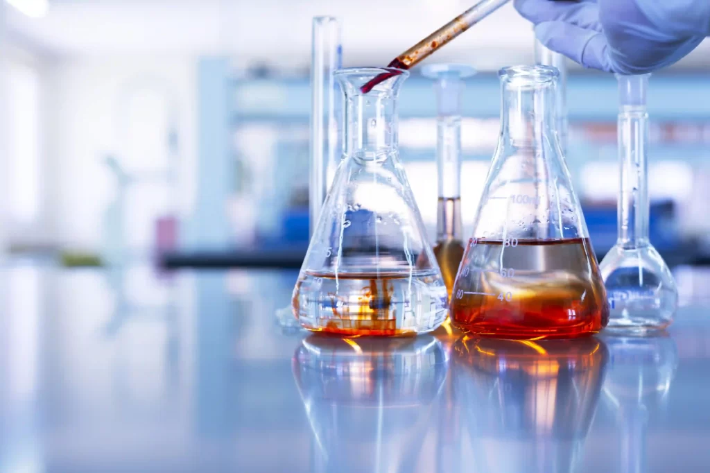 Close-up image from a laboratory setting of a researcher's hands filling various test labware such as tubes and flasks with a pipette.