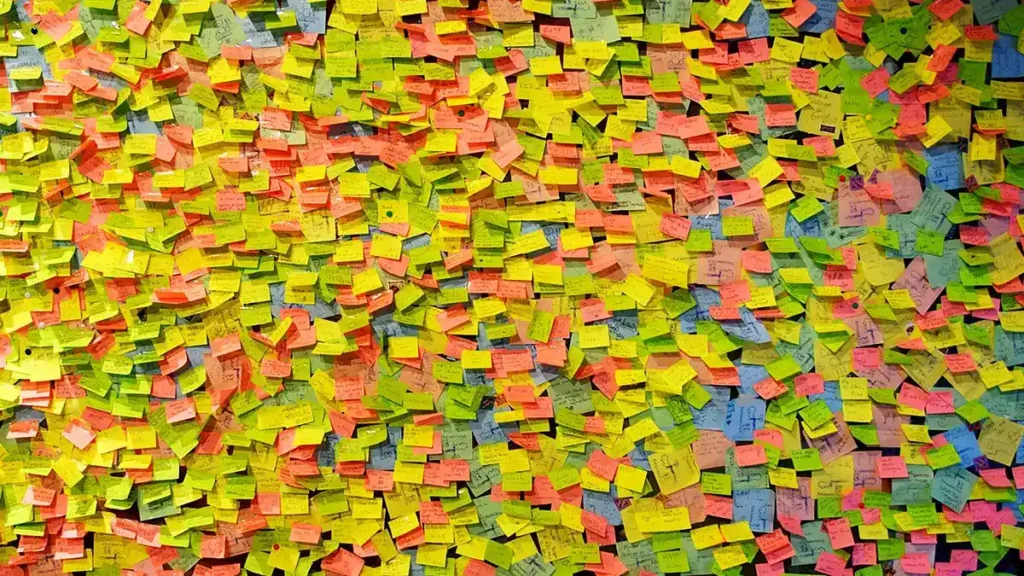 A vibrant collage of sticky notes in various colors, including yellow, green, pink, and orange, densely arranged on a surface, with handwritten notes visible on many of the notes.