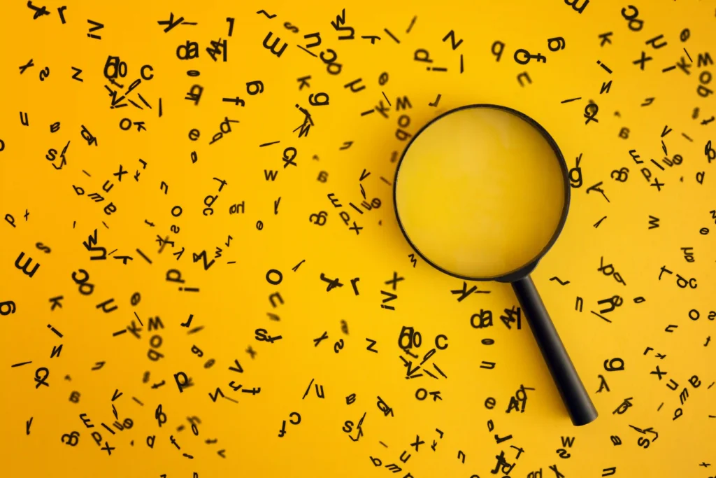Magnifying glass on a yellow background surrounded by scattered black letters, symbolizing the process of keyword search and the importance of keywords in SEO.