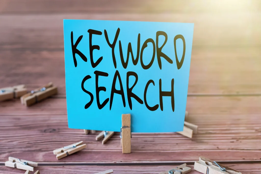 Blue paper note with the words 'Keyword Search' clipped on a wooden stand, highlighting the importance of keyword research in SEO.