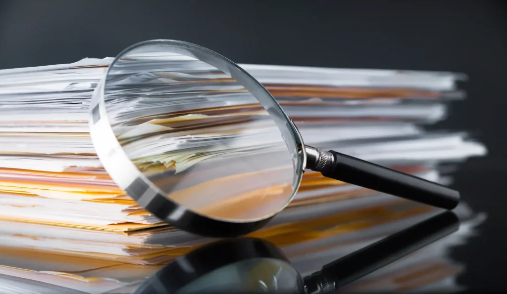A magnifying glass placed over a stack of documents, symbolizing detailed analysis, research, and the process of finding valuable keywords.