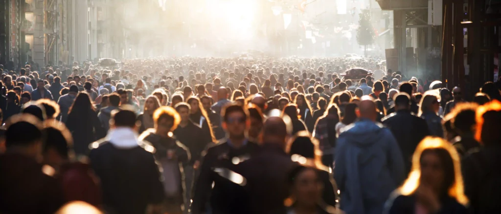 A dense crowd walking through a city street at sunset, symbolizing the importance and challenge of identifying the right audience in communication.
