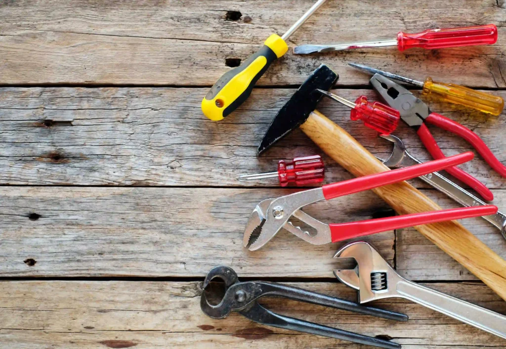 A set of hand tools including pliers, screwdrivers, hammer, and wrench placed on a wooden surface, symbolizing essential tools and resources