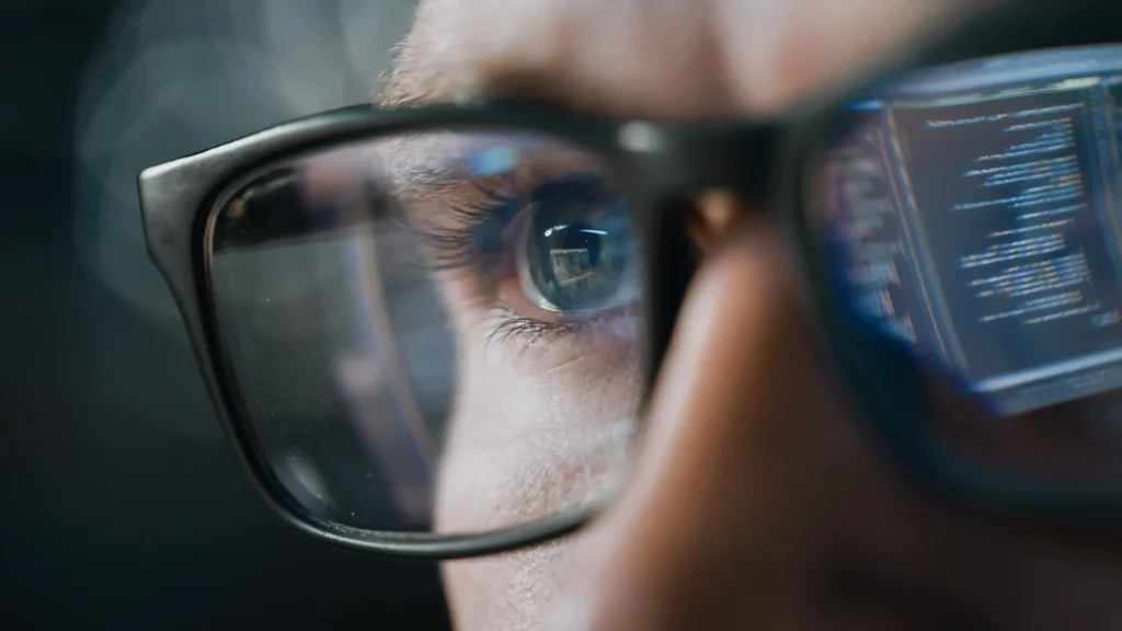 Close-up of eye with code reflected in glasses, representing cybersecurity, monitoring, and protection of digital infrastructure.